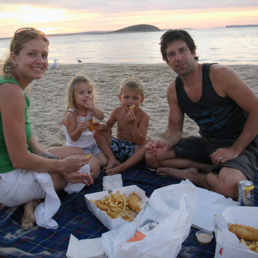 A family having fish and chips on a beach towel at golden hour