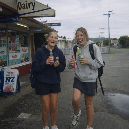 Two friends walking back from the corner shop with cold drinks on a bright day