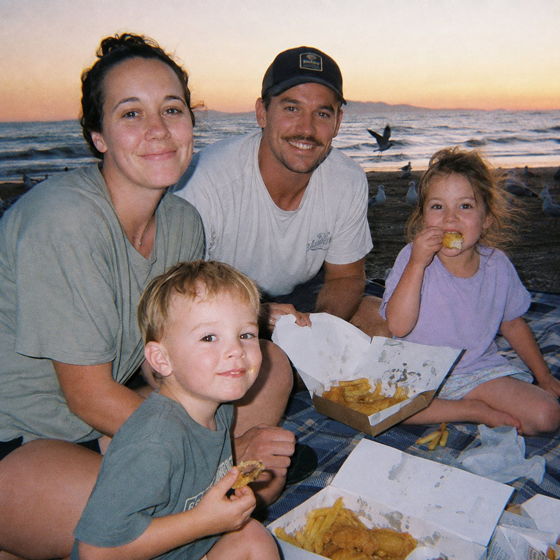 A family eating fish and chips on the beach at sunset, warm grainy tones