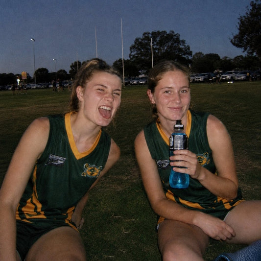 Two teammates laughing on the oval after a game, late afternoon light