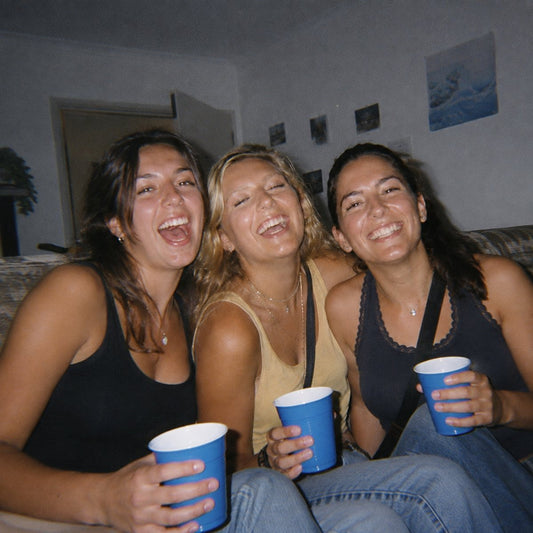 Three friends laughing with cups at a house party, on-camera flash