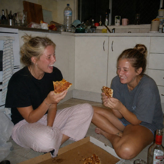 Two friends eating pizza on a kitchen floor late at night, hard on camera flash