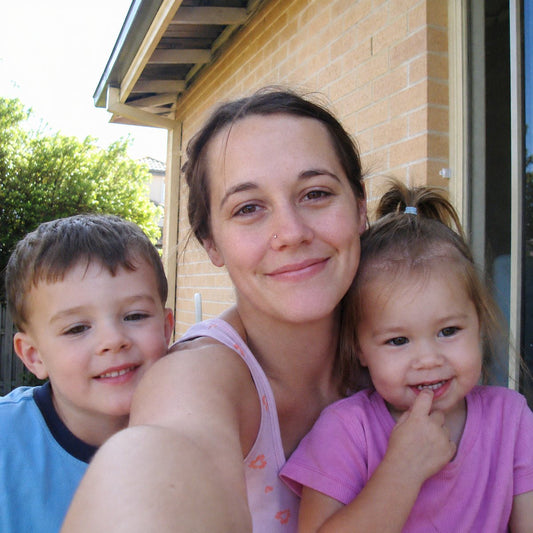 A parent and two young kids squeezed into a selfie on the front porch, hard flash and warm grain