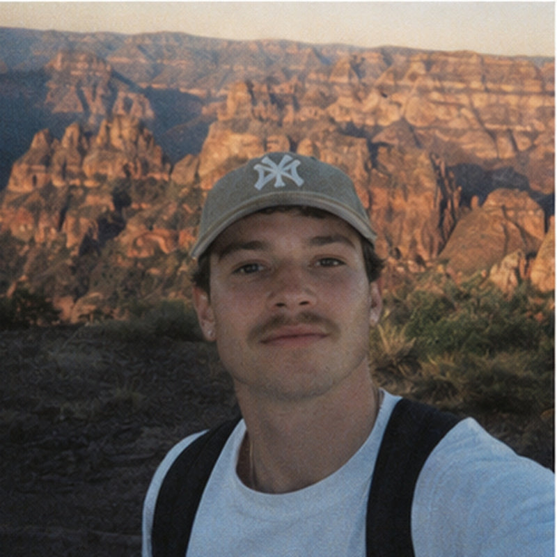 Man in a cap hiking with red rock cliffs behind, warm retro digicam style travel photo