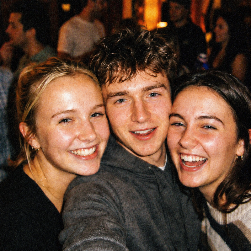 Three friends squeezed into a night time selfie, lit by hard on camera flash