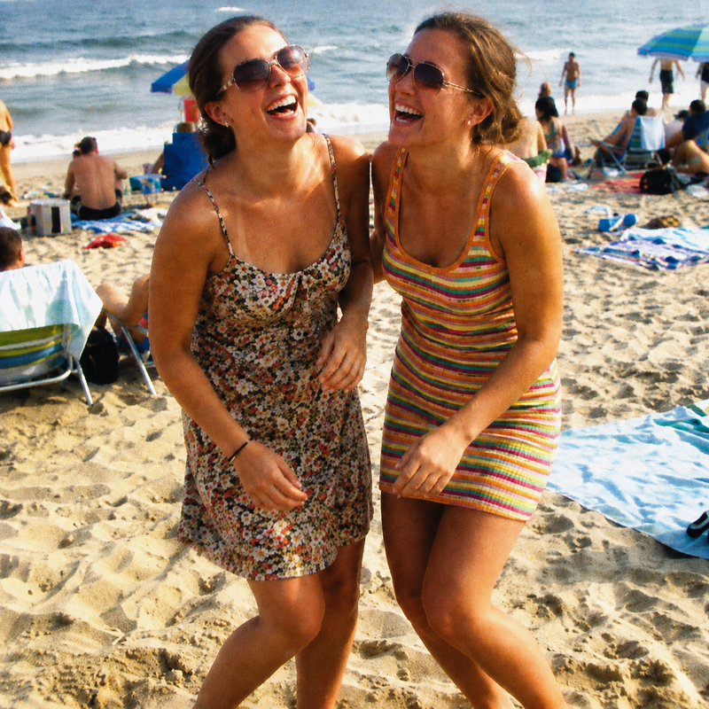 Two friends laughing in the sand on a busy summer beach