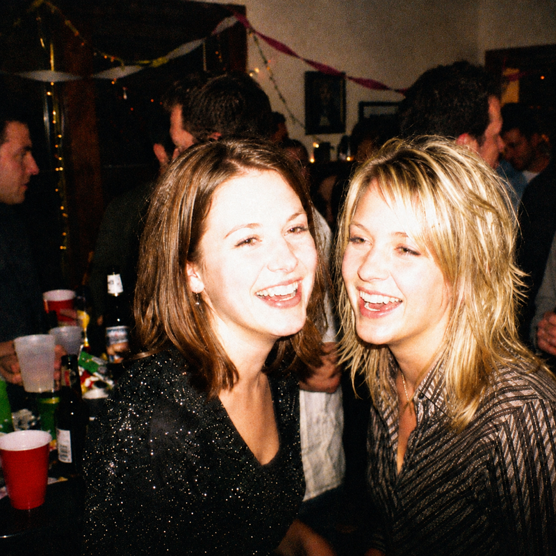 Two friends at a house party at night, lit by on camera flash