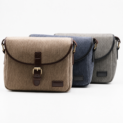 Three textured canvas messenger bags in beige, navy, and gray, arranged in a row against a clean white background.