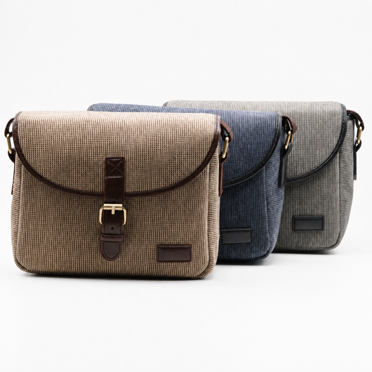 Three textured canvas messenger bags in beige, navy, and gray, arranged in a row against a clean white background.