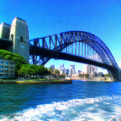 Sydney Harbour Bridge over blue water with the Sydney skyline in the background under a clear blue sky.