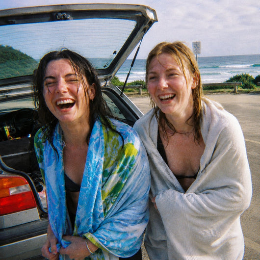 Two friends laughing in towels at the back of a car after a swim